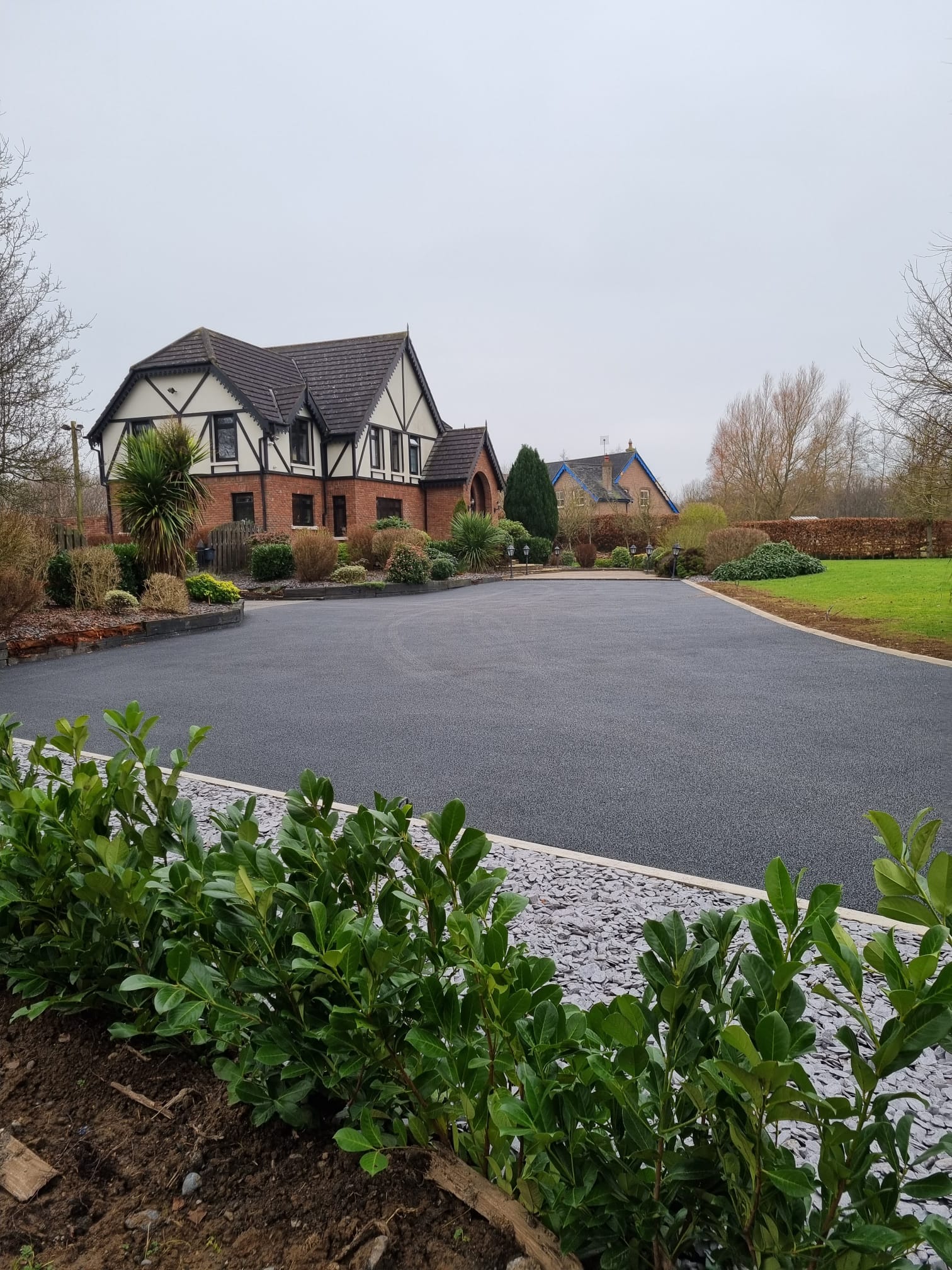 Premium tarmacadam driveway at a brick Tudor country house with planted island and granite cobble bands, Delaney Tarmac install